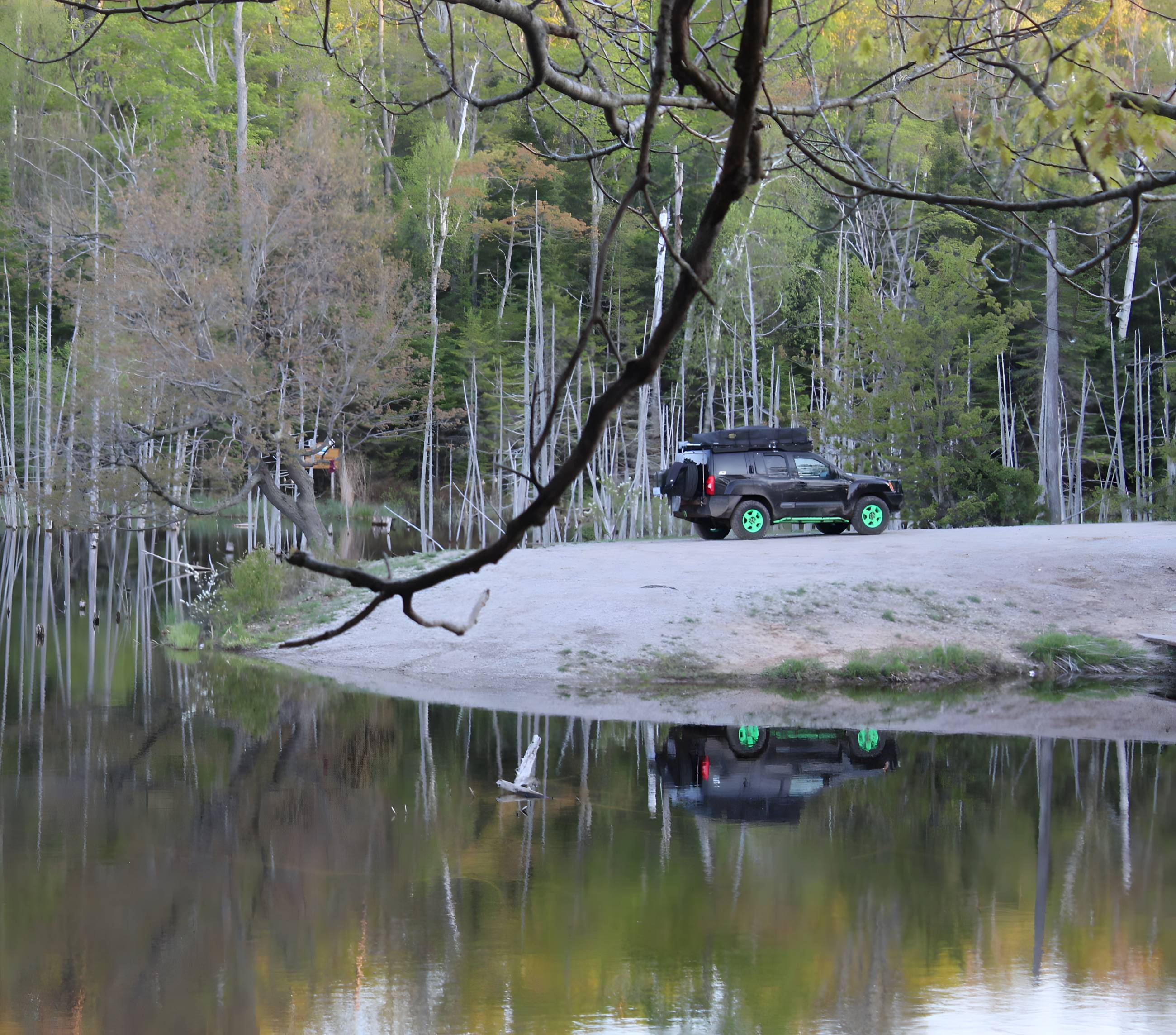 Truck parked on a sandy riverbank reflected in still water