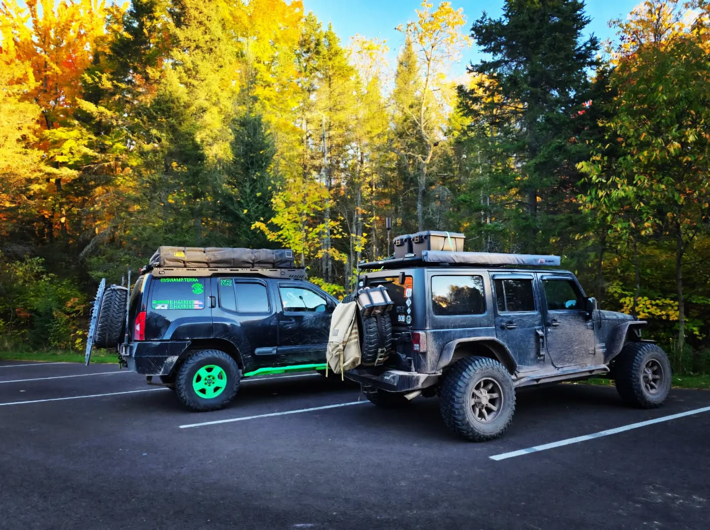 Two expedition trucks under bright autumn trees